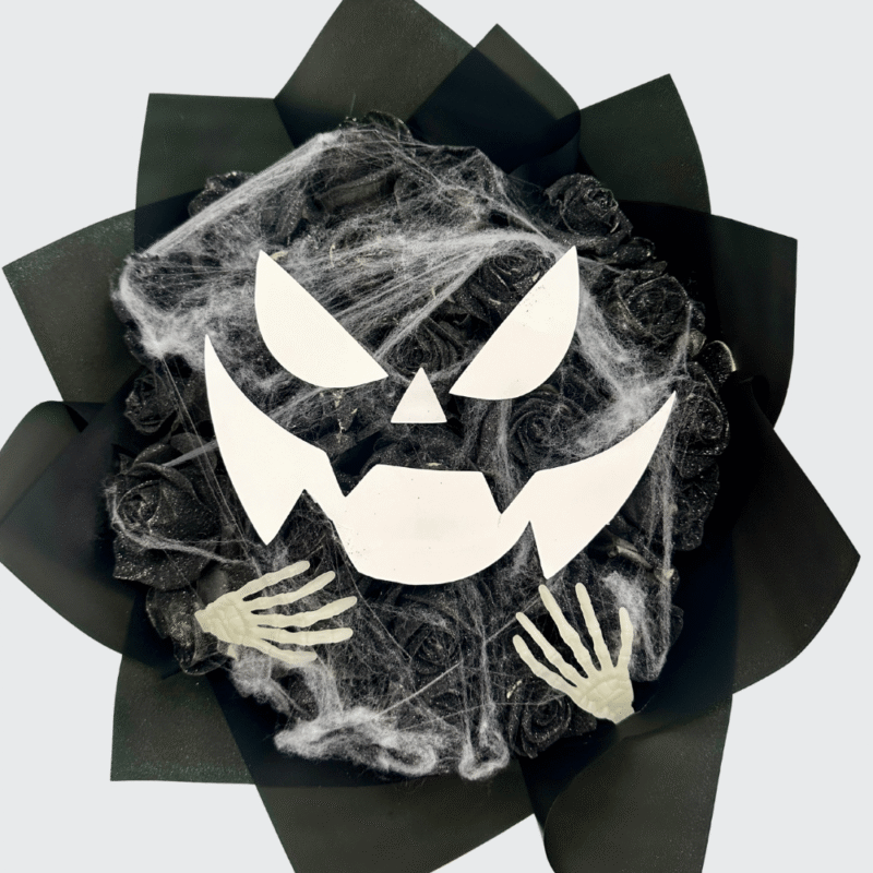 Halloween bouquet with black roses arranged in the shape of a monster face, featuring spider webs and skeleton hands β spooky floral design by Frutidetails Miami.