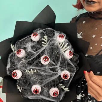Halloween black flower bouquet with eyeball decorations, spider webs, and skeleton hands — spooky floral arrangement by Frutidetails Miami.