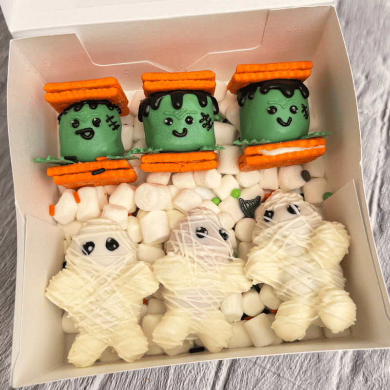 Halloween chocolate box with Frankenstein and mummy characters made from decorated chocolate-covered cookies and marshmallows β handcrafted by Frutidetails Miami.