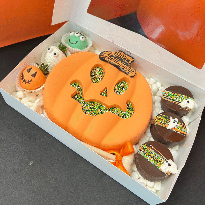 Breakable chocolate pumpkin heart filled with candies, Halloween-themed strawberries, and chocolate-covered cookies β handcrafted by Frutidetails Miami.