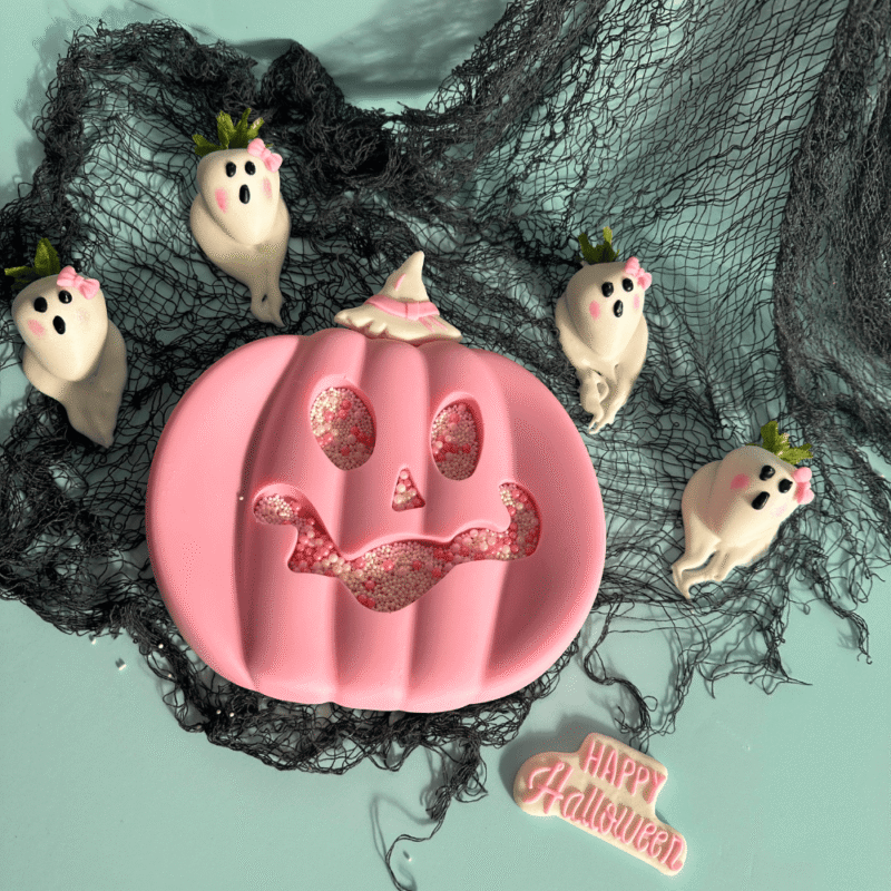 Pink breakable chocolate pumpkin heart surrounded by ghost-shaped chocolate-covered strawberries β handcrafted Halloween gift by Frutidetails Miami.